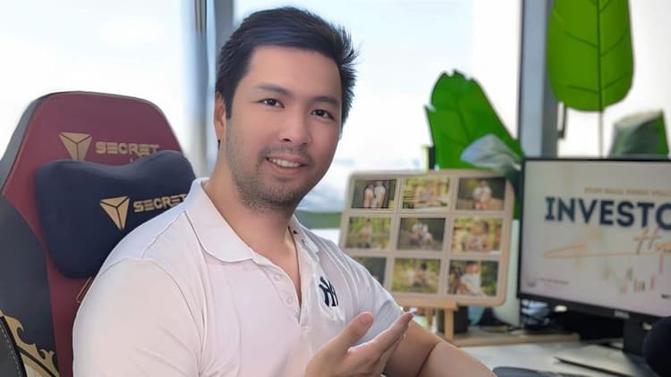 Hendry Tanadi smiling at his desk with “Investors Handbook” displayed on a computer screen.