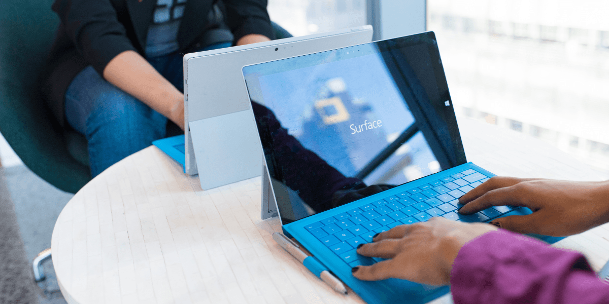 Two people using Microsoft Surface laptops at a table in a modern setting