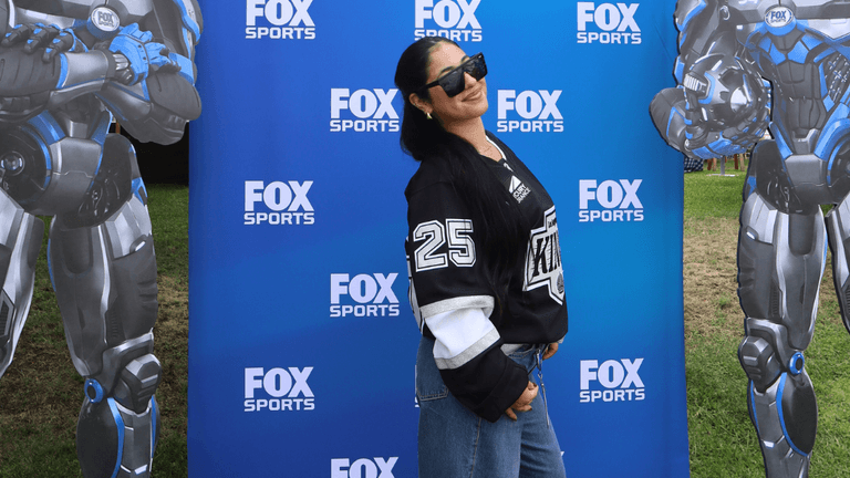 Olivia Weinstock poses at FOX Sports event with futuristic robot cutouts on each side.