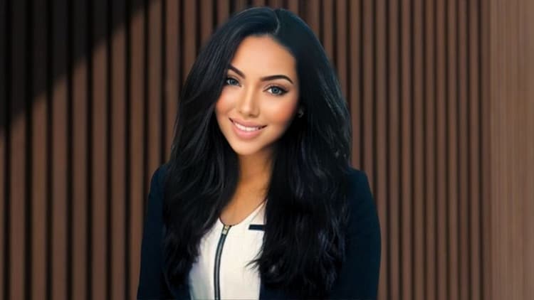 Portrait of a confident woman in a business suit, smiling with long black hair, standing in front of a brown wooden wall, conveying professionalism and elegance.