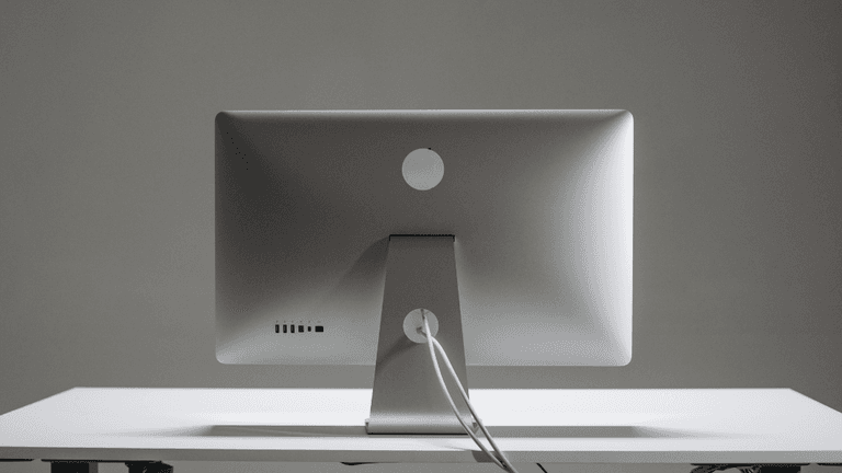 Back view of a sleek silver computer monitor on a minimalist white desk
