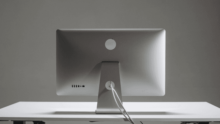 Back view of a sleek silver computer monitor on a minimalist white desk