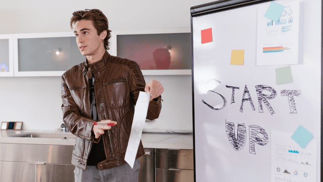 Young man presenting by a whiteboard with "START UP" written on it
