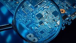 Close-up of a circuit board viewed through a magnifying glass against a blue background