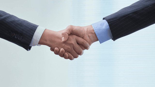 Two business professionals shake hands in a professional setting.