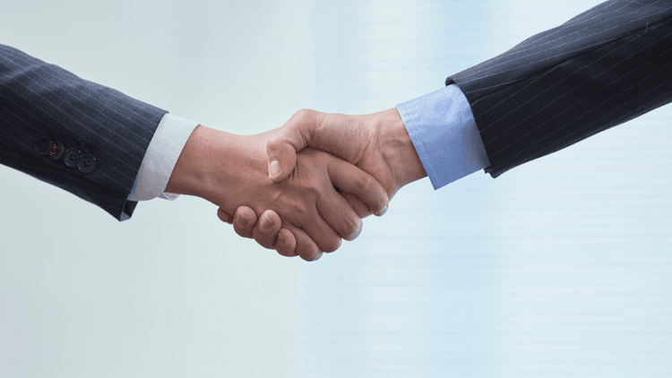 Two business professionals shake hands in a professional setting.