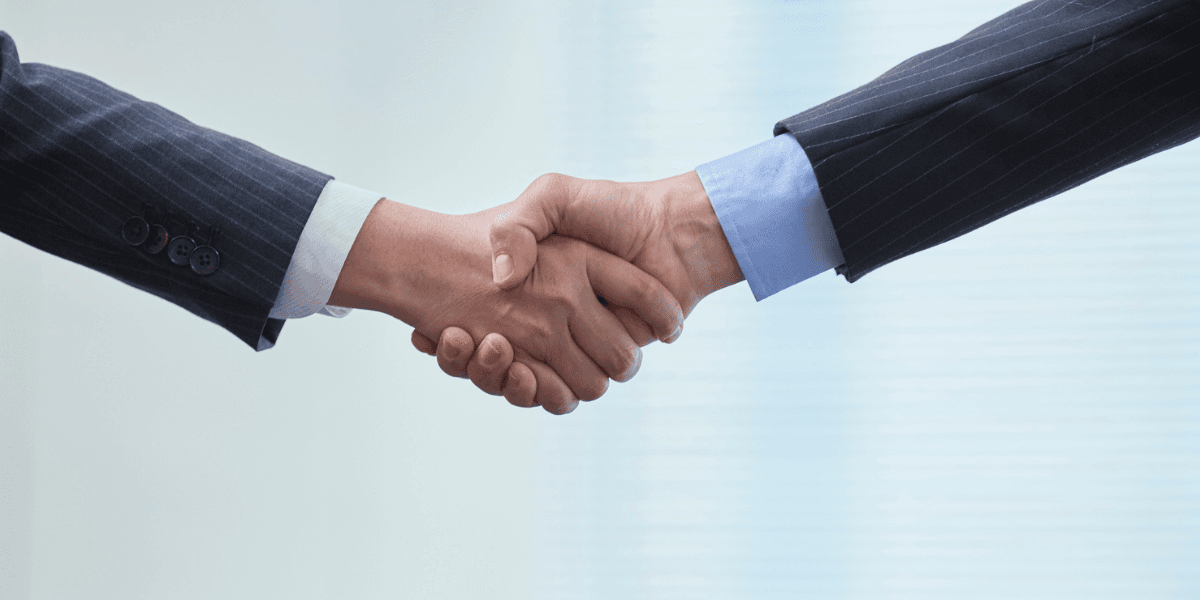 Two business professionals shake hands in a professional setting.
