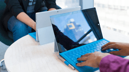 Two people using Microsoft Surface laptops at a table in a modern setting