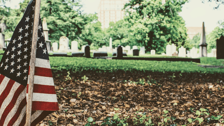 American flag placed in a cemetery among gravestones and fallen leaves