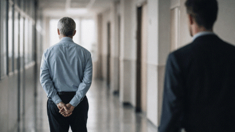 A senior and junior professional walking down a hallway, representing mentorship and generational knowledge transfer.