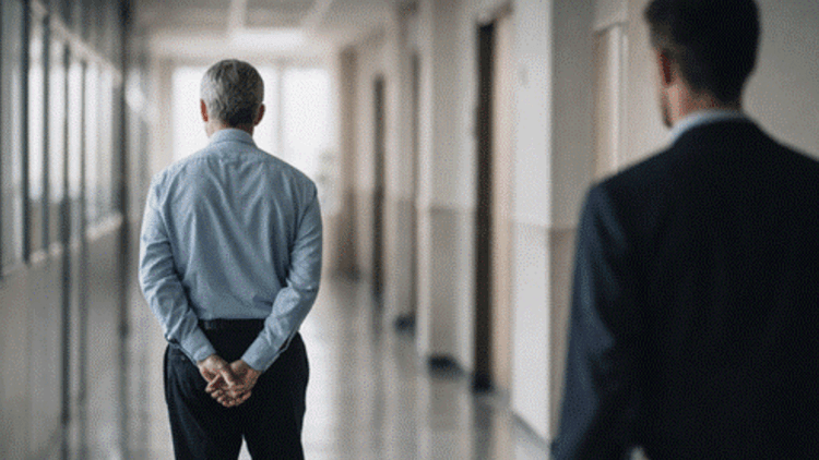 A senior and junior professional walking down a hallway, representing mentorship and generational knowledge transfer.