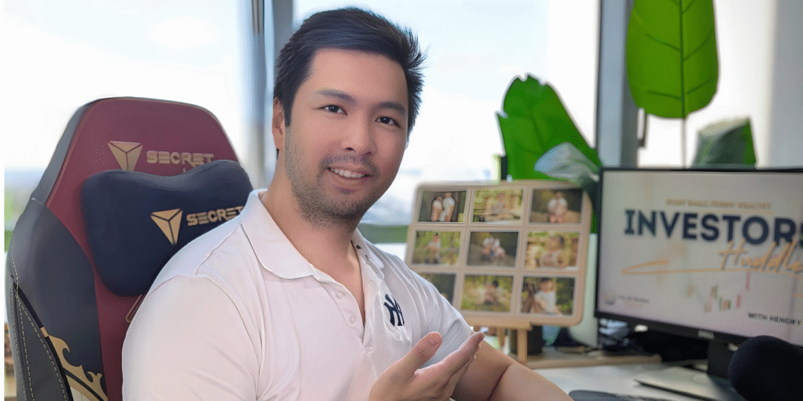 Hendry Tanadi smiling at his desk with “Investors Handbook” displayed on a computer screen.