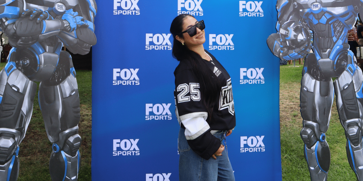 Olivia Weinstock poses at FOX Sports event with futuristic robot cutouts on each side.