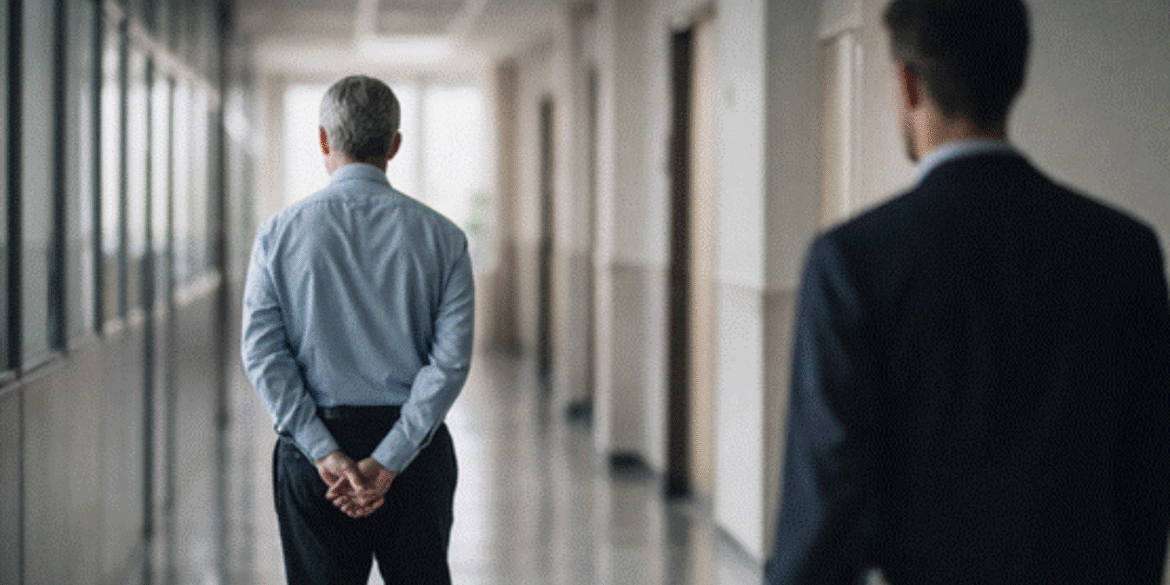 A senior and junior professional walking down a hallway, representing mentorship and generational knowledge transfer.